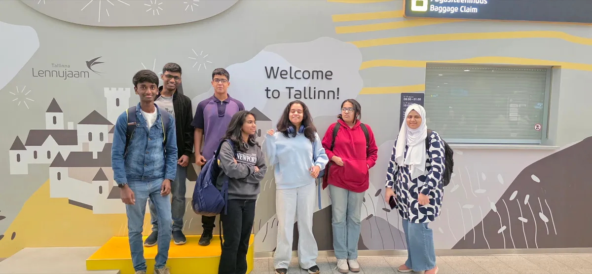 A group of students from India standing in front of a wall that reads Welcome to Tallinn at Tallinn Airport.