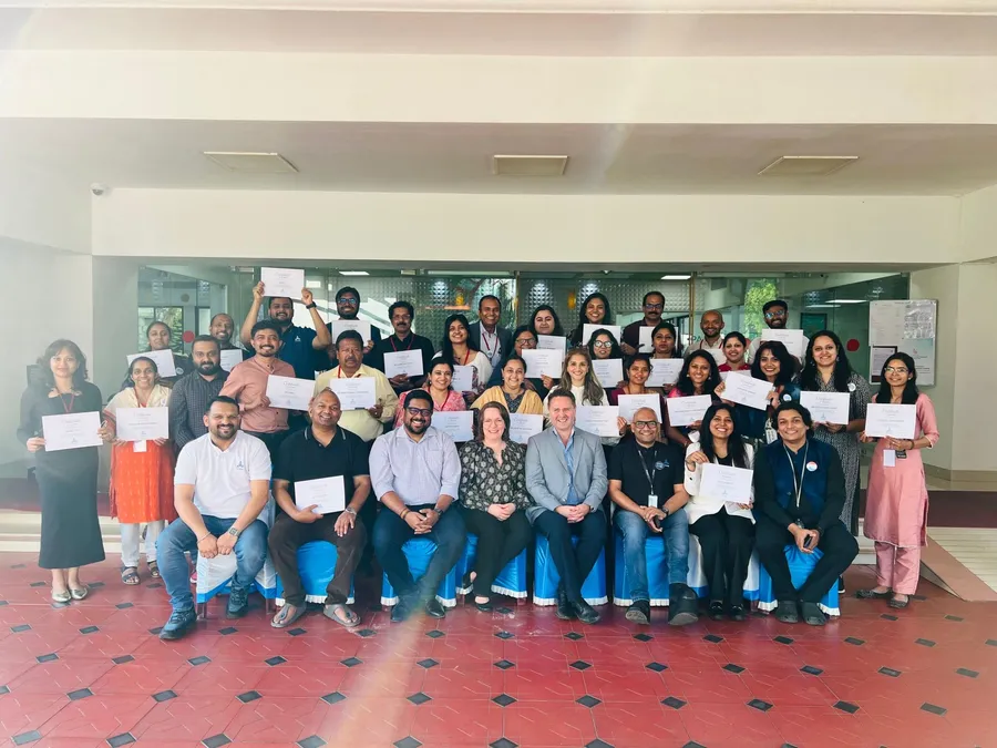 A large group of educators holding certificates, with Finnish trainers seated in the front row.