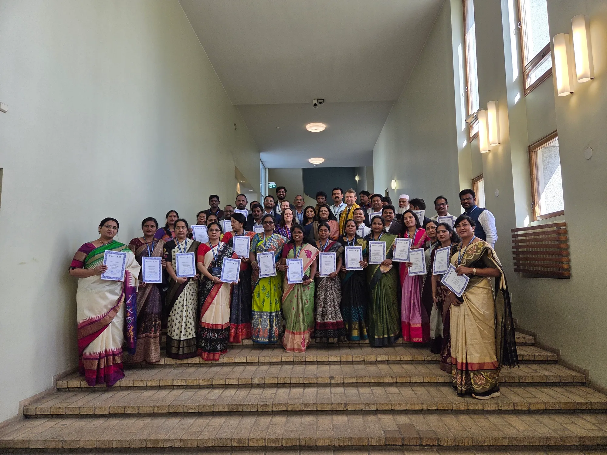 A delegation of teachers standing on a staircase, each holding a certificate.