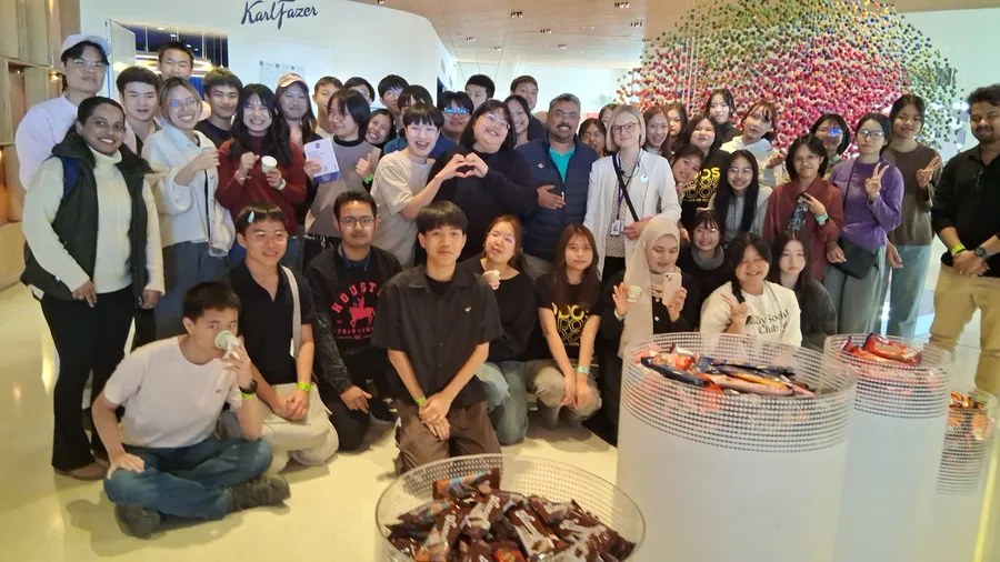 A large student group from Thailand with their hosts in the Fazer visitor centre, with bowls of chocolate in the foreground.