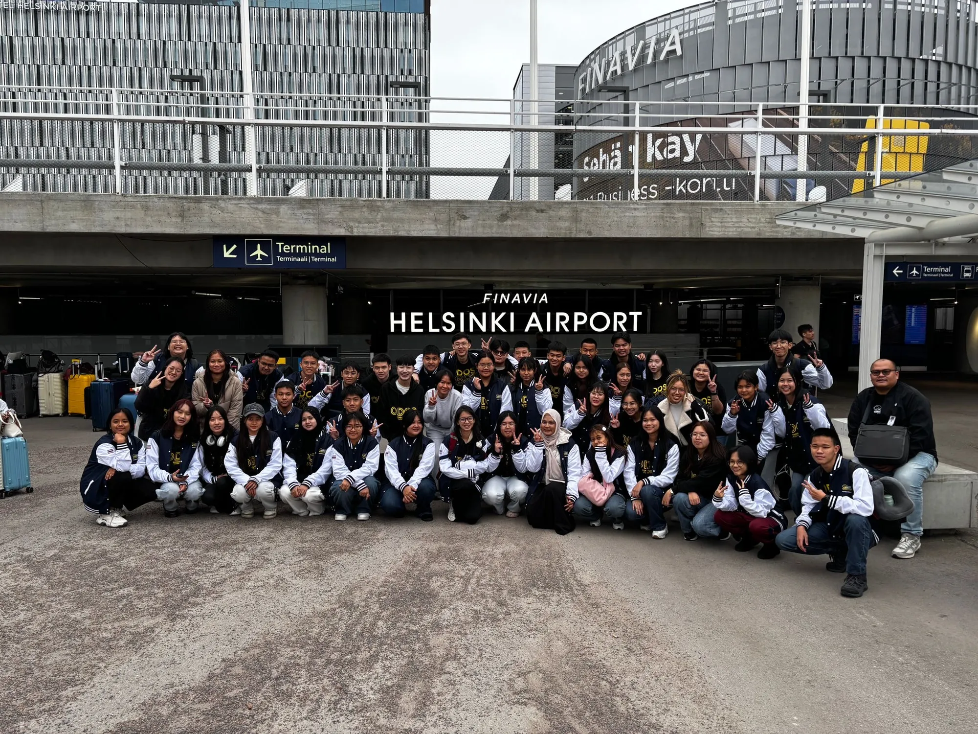 A student group from Thailand in matching jackets outside the terminal at Helsinki Airport.